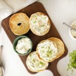 overhead view of an askew wooden cutting board with 2 halved bagels with flavored cream cheese on top.