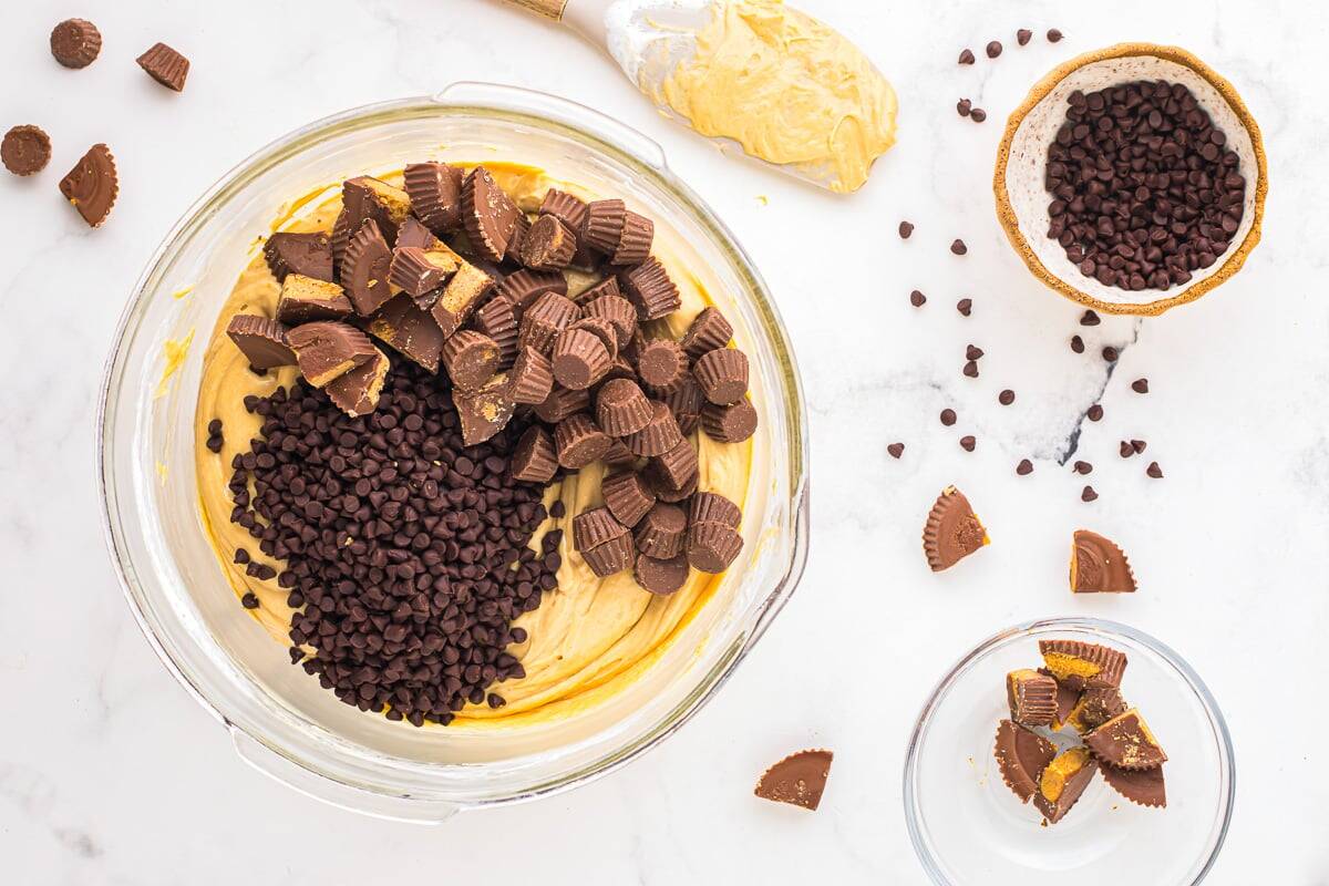 chopped peanut butter cups and chocolate chips over peanut butter fluff in a glass bowl.