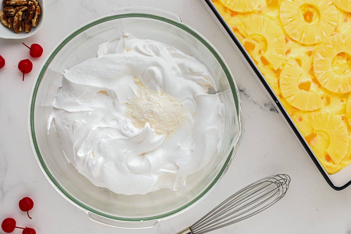 adding pudding mix to whipped topping in a glass bowl.