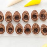 cooled egg-shaped brownies with hollowed-out yolk centers, surrounded by creme filling in piping bags.