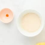 creme filling mixed in a white bowl next to a small bowl with a dot of yellow food coloring.