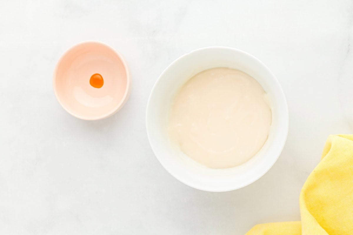 creme filling mixed in a white bowl next to a small bowl with a dot of yellow food coloring.