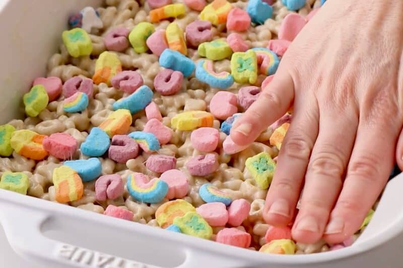 Pressing Lucky Charms marshmallows into cereal bar mixture.
