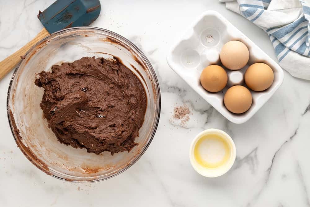Brownie cookie dough in a mixing bowl, next to carton of eggs.