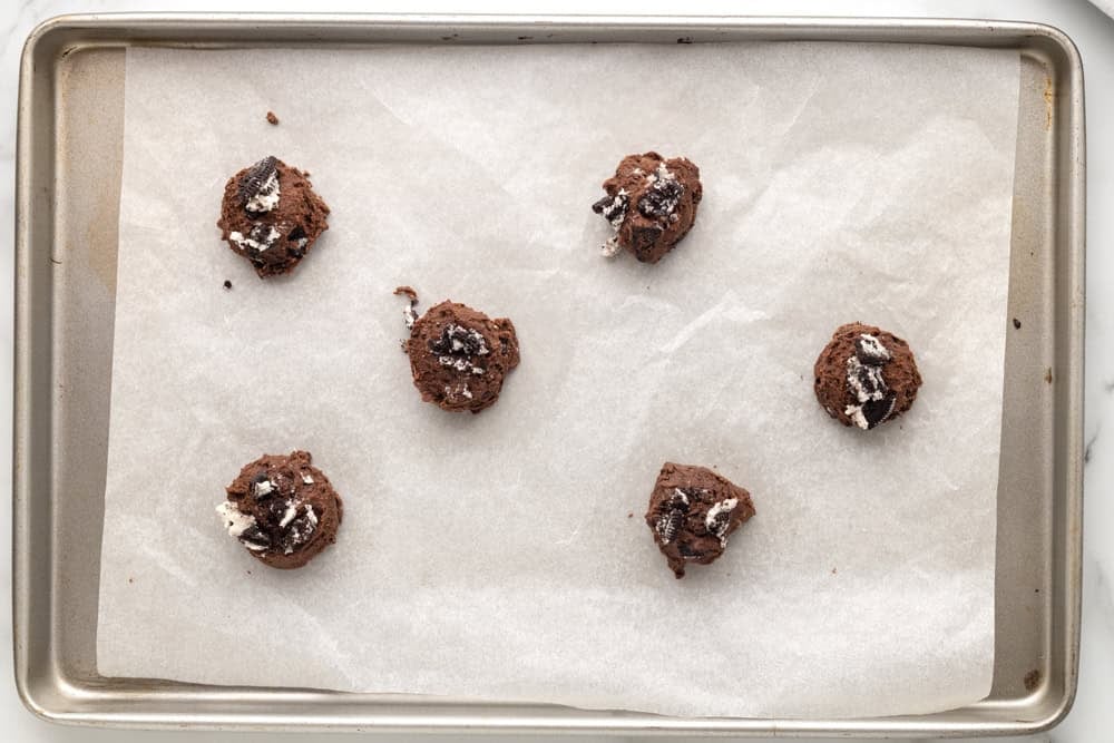 Oreo brownie cookie dough balls lined up in a baking tray lined with parchment.