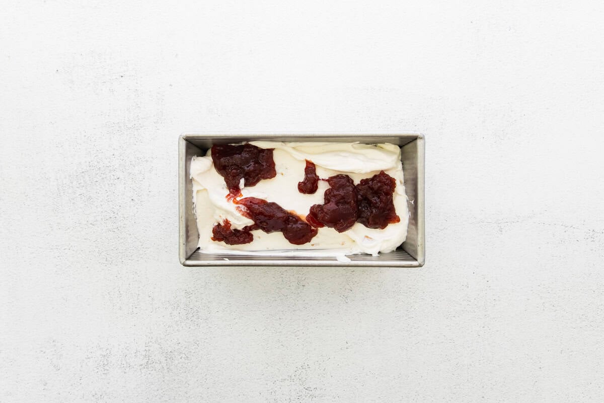 Cream cheese ice cream poured into a loaf pan, with strawberry jam added on top.