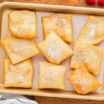 Nine baked sopapillas on a baking sheet.