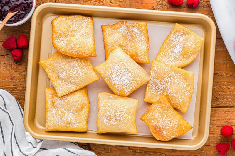 Nine baked sopapillas on a baking sheet.