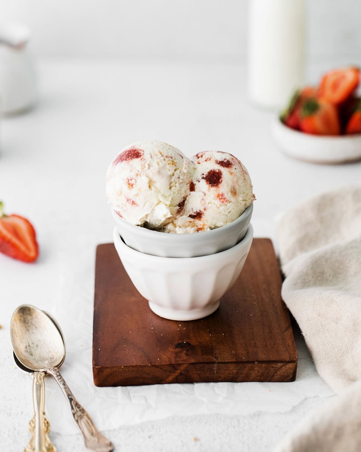 Scoops of homemade strawberry cheesecake ice cream served in a bowl next to two spoons.