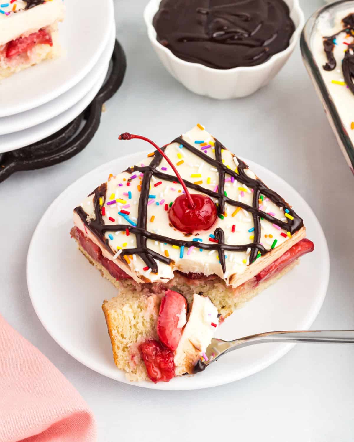 Banana split cake with strawberries and frosting served on a plate.
