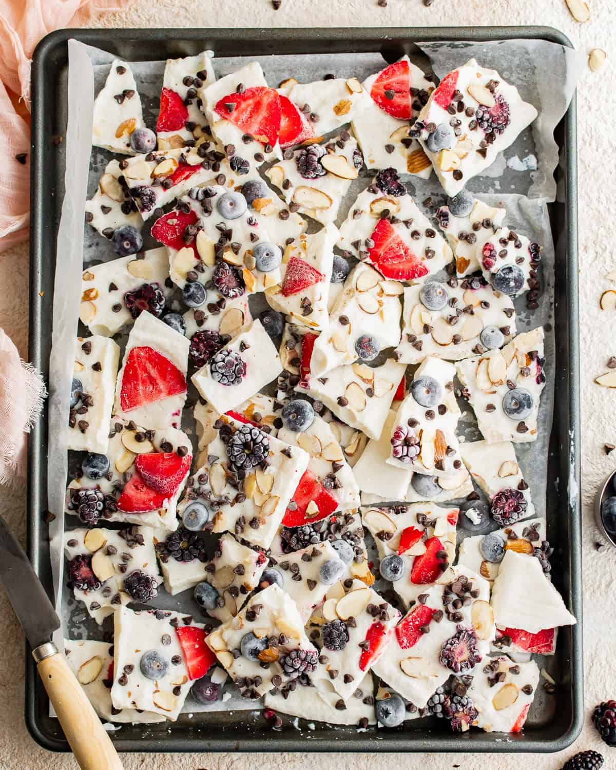 Broken frozen yogurt bark pieces, filled with berries and nuts in a baking tin.
