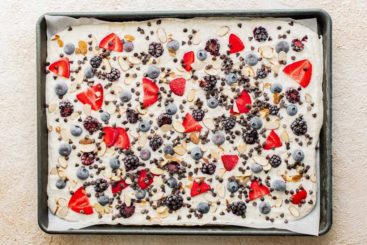 Frozen yogurt bark scattered with berries and fruit, before breaking it apart.