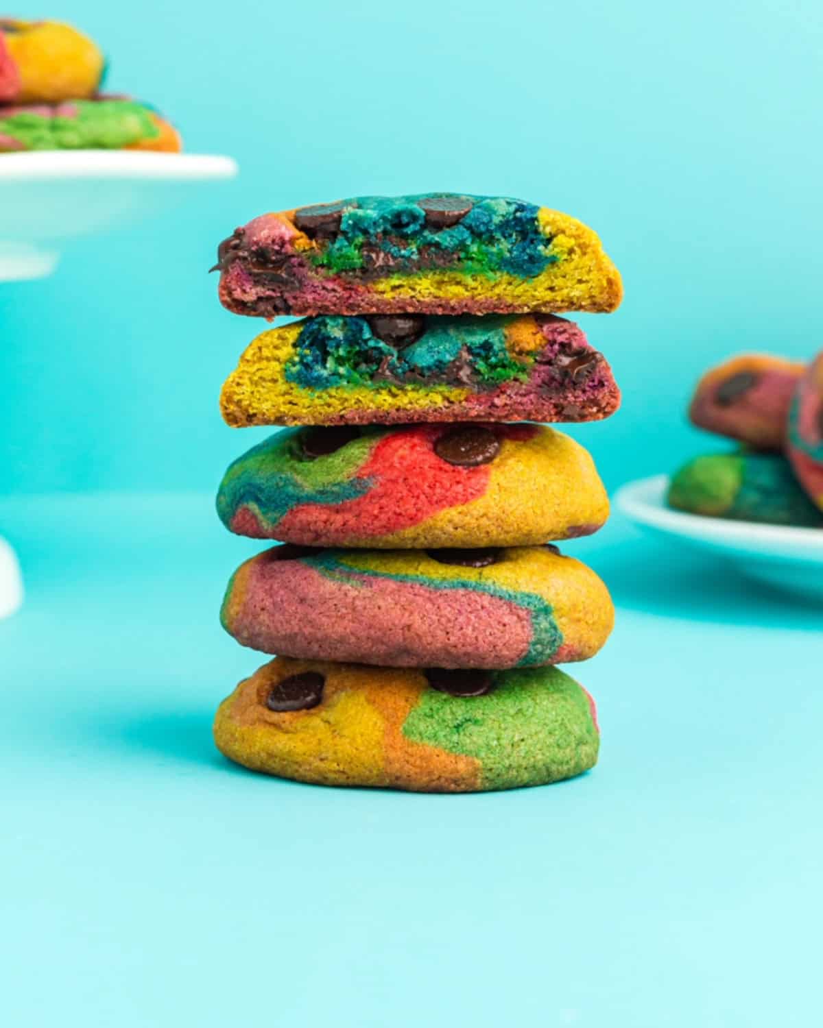 A stack of rainbow chocolate chip cookies against a neon blue background.