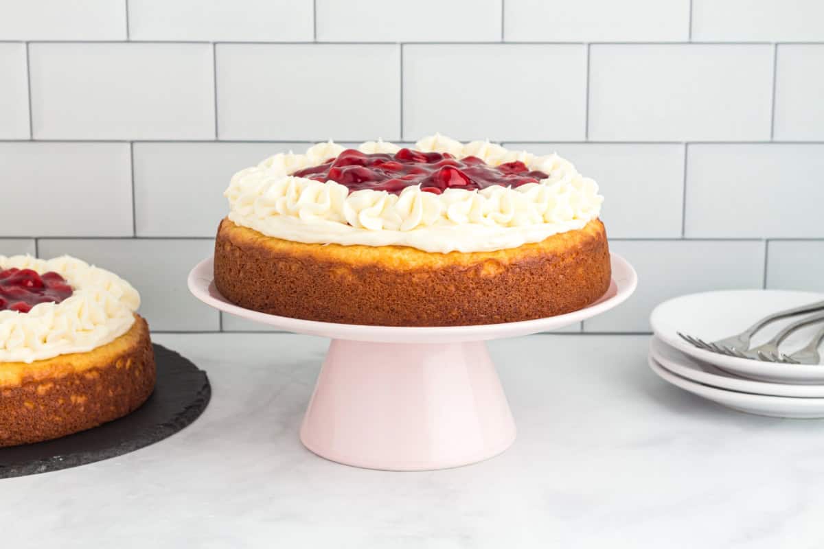 Round cherry topped cake on a cake stand, viewed from the side.