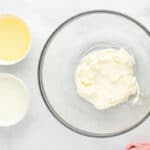 Beaten cream cheese in a glass mixing bowl surrounded by ingredients.