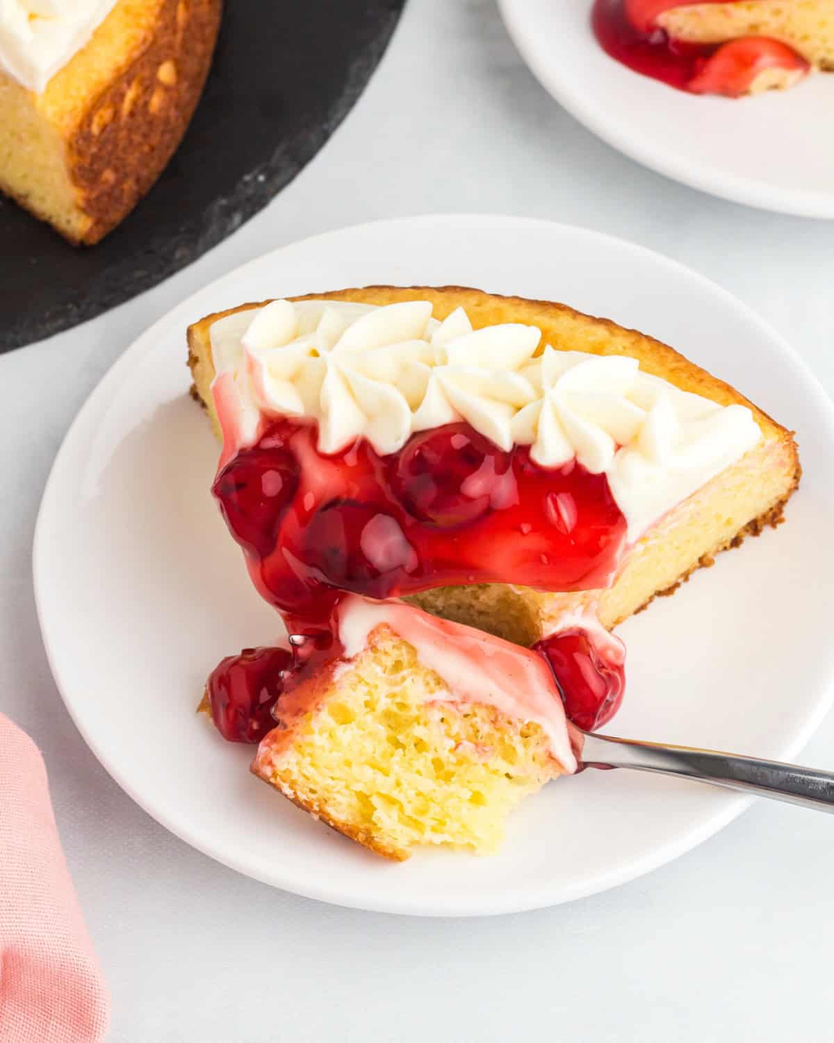 A slice of cherry cheesecake cake on a white place with a fork digging in.