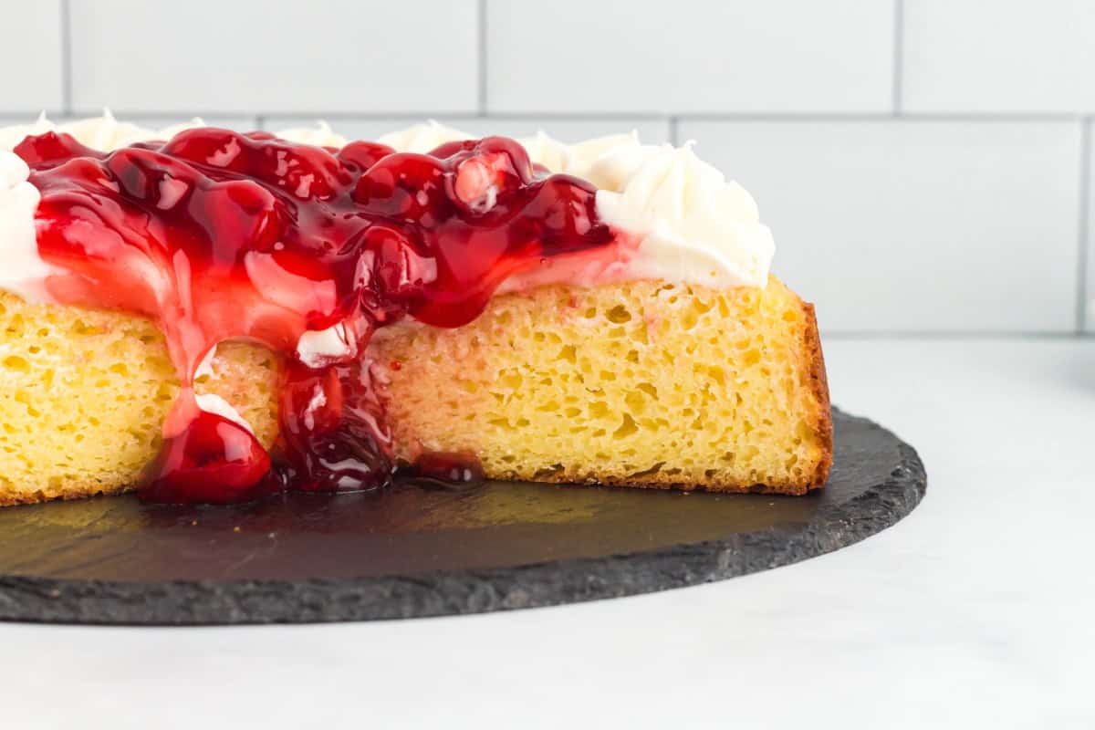 Cherry pie filling spilling over a sliced cheesecake cake.