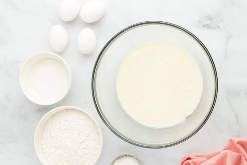 Beaten cream cheese, milk, and vegetable oil in a glass mixing bowl surrounded by ingredients.