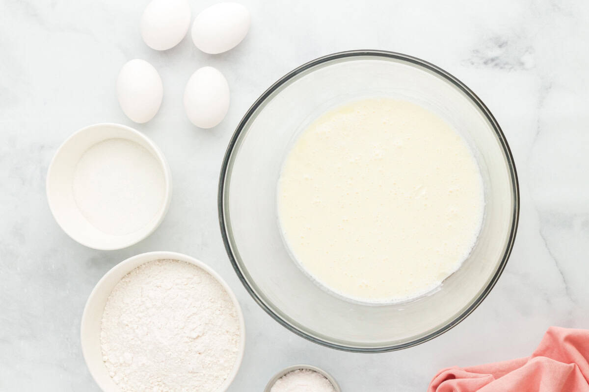 Beaten cream cheese, milk, and vegetable oil in a glass mixing bowl surrounded by ingredients.