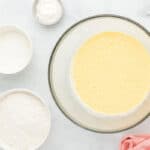 Beaten cream cheese, milk, oil, and eggs in a glass mixing bowl surrounded by ingredients.