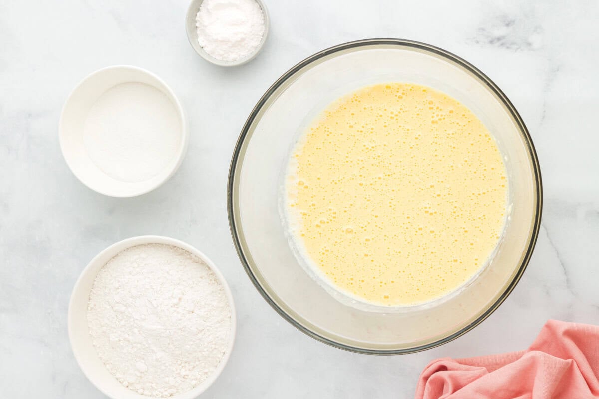 Beaten cream cheese, milk, oil, and eggs in a glass mixing bowl surrounded by ingredients.