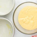 Cherry cheesecake cake batter in a glass mixing bowl beside two empty cake pans.