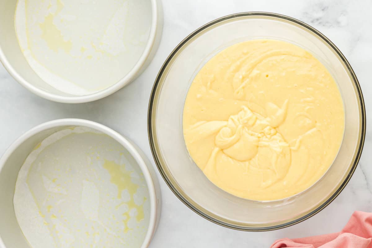 Cream cheese cake batter in a glass mixing bowl beside two empty cake pans.