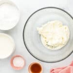 Beaten cream cheese in a glass mixing bowl surrounded by ingredients.