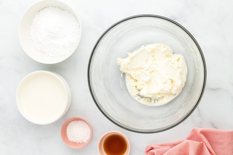 Beaten cream cheese in a glass mixing bowl surrounded by ingredients.