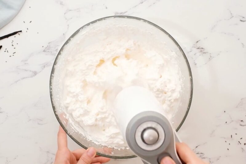 Whipping cream in a glass mixing bowl, using a hand mixer.