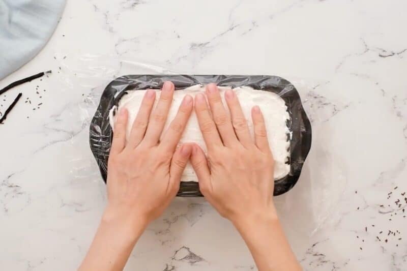 Pressing plastic wrap over a pan of no churn ice cream.