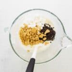 Folding crushed graham crackers, marshmallows, and chocolate chips into cream mixture.