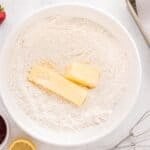 Sticks of butter added to a bowl of flour.