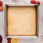 Shortbread crust for strawberry crumble bars in a square baking pan.