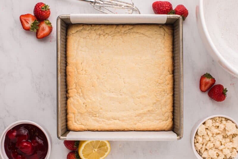 Shortbread crust for strawberry crumble bars in a square baking pan.
