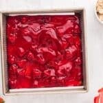 A layer of strawberry pie filling in a square baking pan.