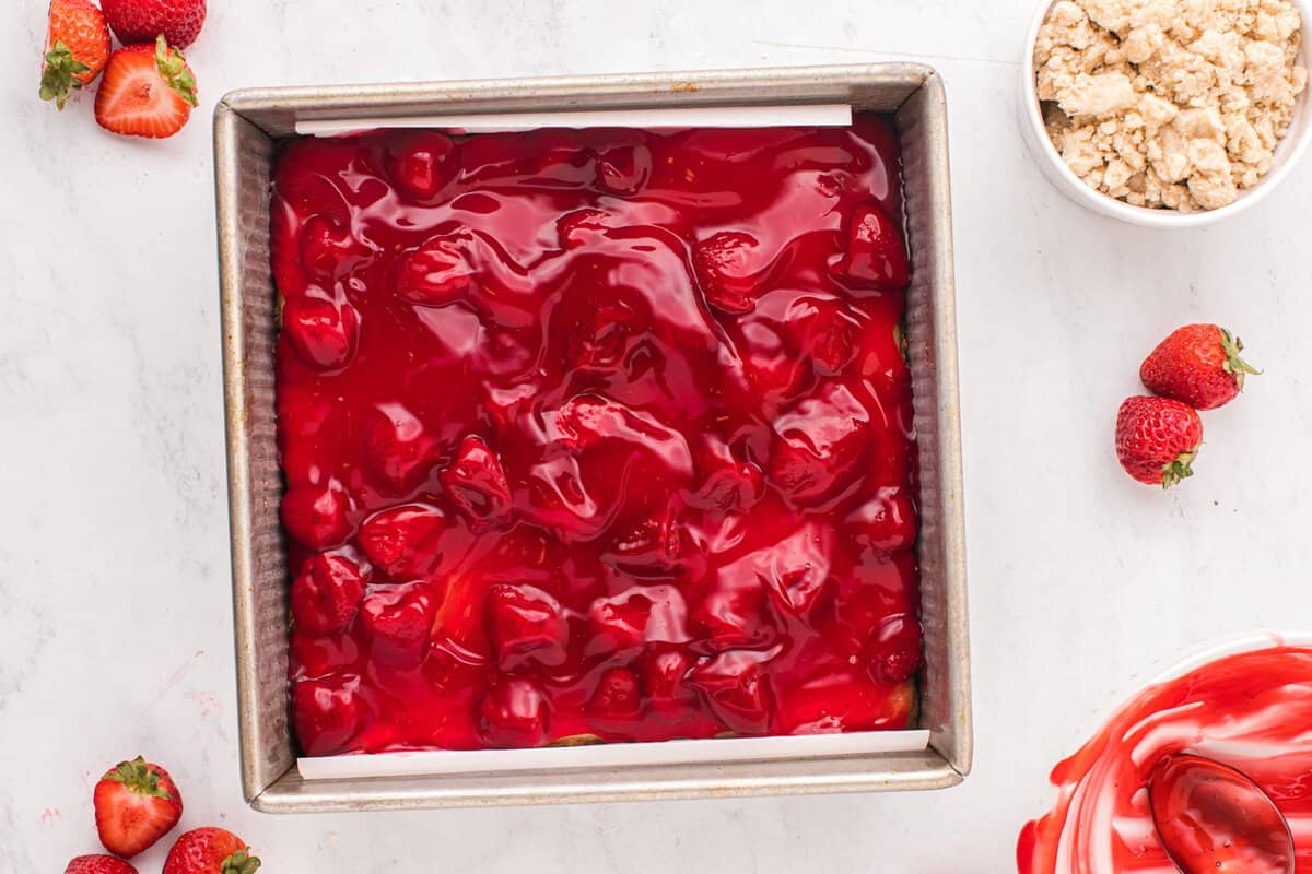 A layer of strawberry pie filling in a square baking pan.