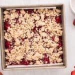 Assembled strawberry crumble bars in a square baking pan.