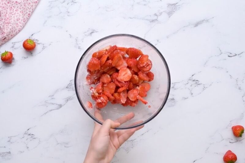 Sliced strawberries coated in sugar, macerating in a glass bowl.