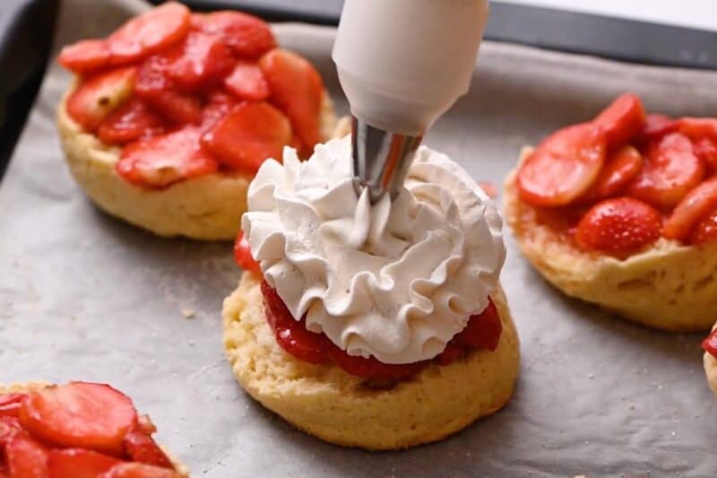 Topping a biscuit and strawberries with whipped cream.