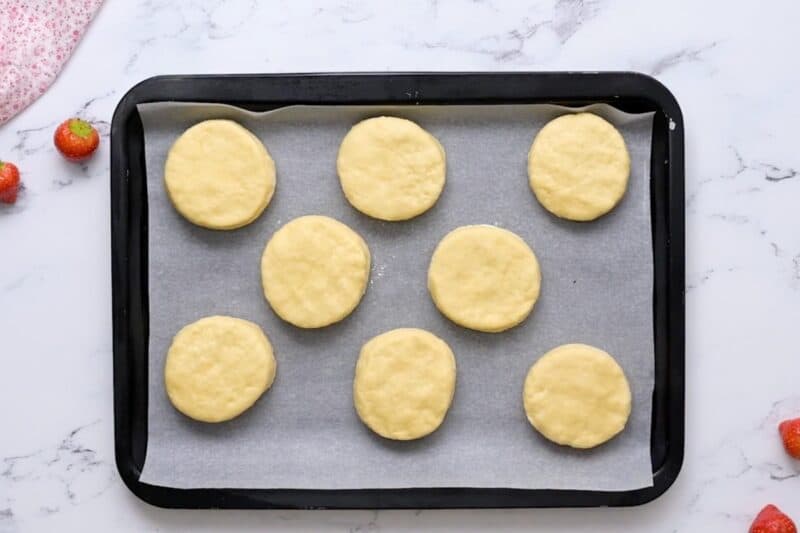 Refrigerated biscuit dough lined up on a baking sheet.