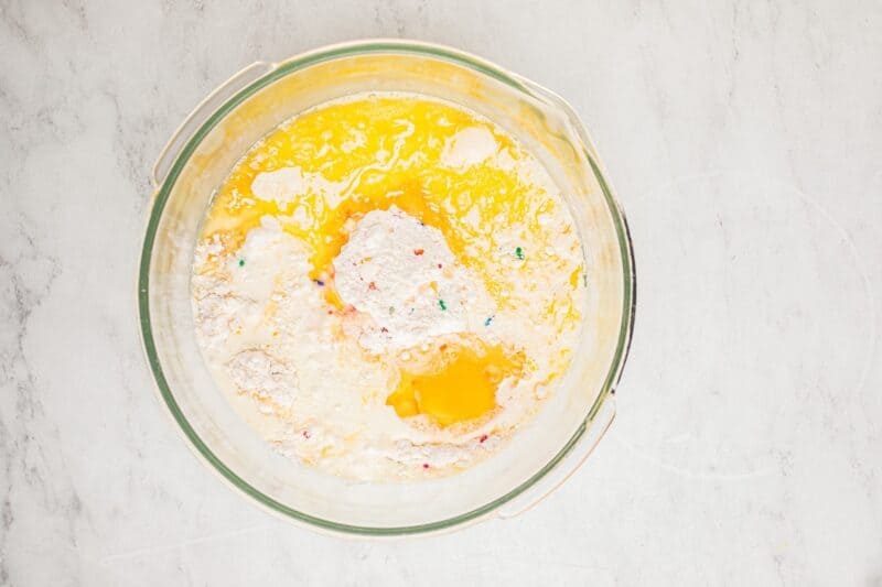 Funfetti cake mix, melted butter, egg, and heavy cream in a glass mixing bowl.