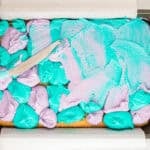 Using a knife to swirl dollops of purple and blue frosting.