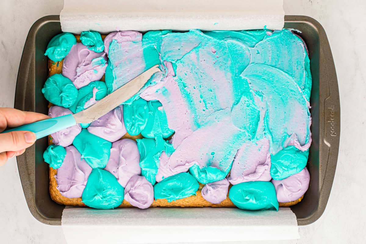 Using a knife to swirl dollops of purple and blue frosting.