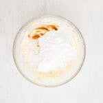 Vanilla extract and powdered sugar in a mixing bowl with beaten cream cheese and butter.