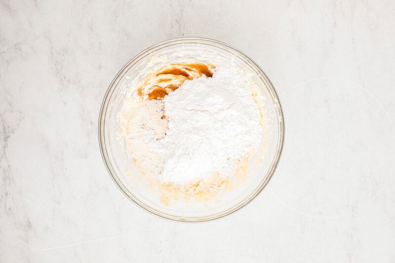 Vanilla extract and powdered sugar in a mixing bowl with beaten cream cheese and butter.