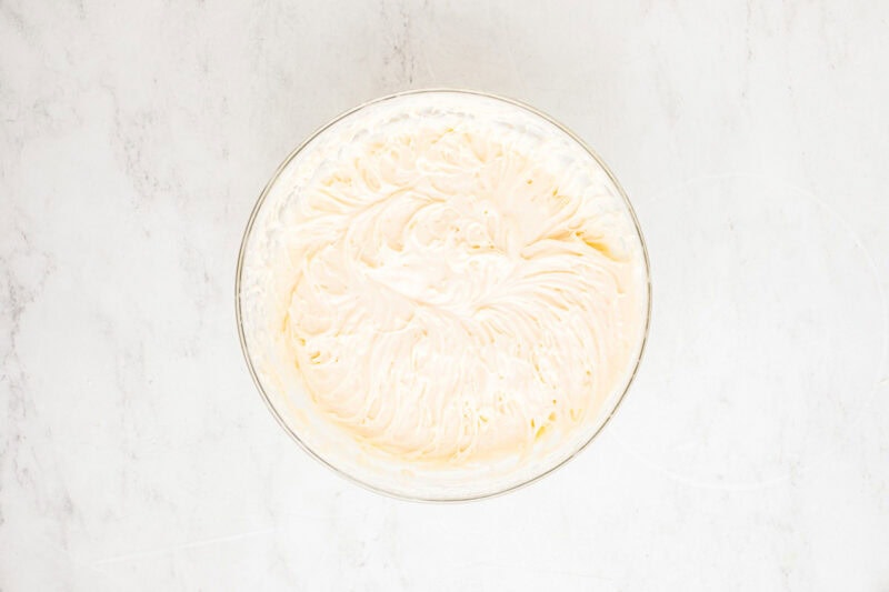 Fluffy cream cheese frosting in a glass mixing bowl.