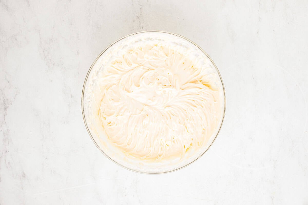 Fluffy cream cheese frosting in a glass mixing bowl.
