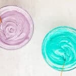 Purple and blue frosting in glass mixing bowls.