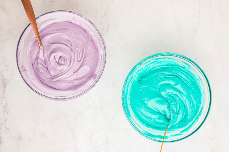 Purple and blue frosting in glass mixing bowls.